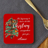 A personalised red square coaster with an illustration of a Christmas tree and the words "it's beginning to look a lot like Chrsitmas" printed onto it. The coaster is customised with the name "Aimee"